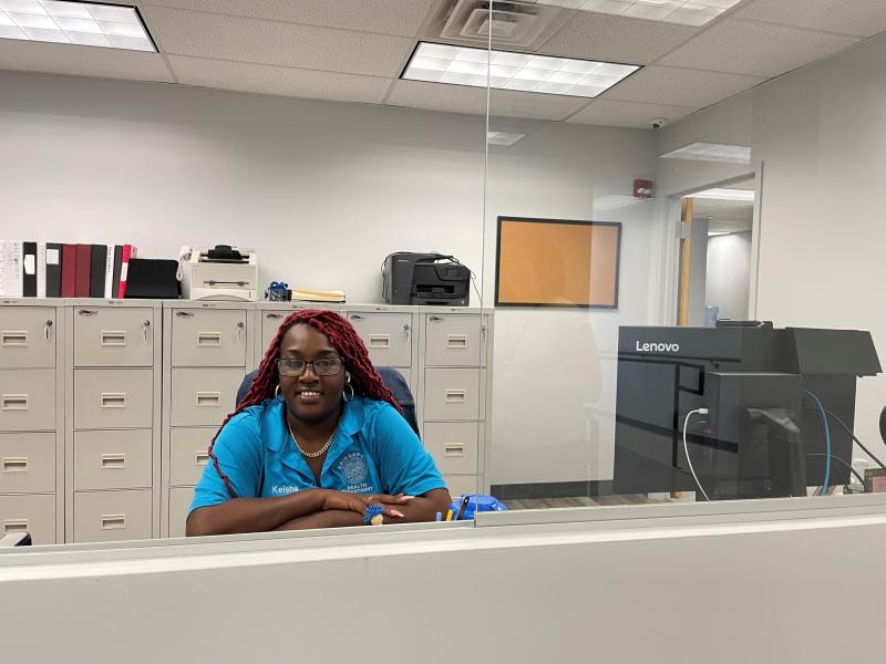 Picture of the receptionist area in the New wellness clinic. The receptionist smiling in the middle, computer to her side, and filling cabinets in the back 