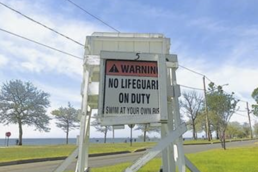 "No Lifeguard on Duty" sign. The white warning sign is outdoors on grass, near a waterfront