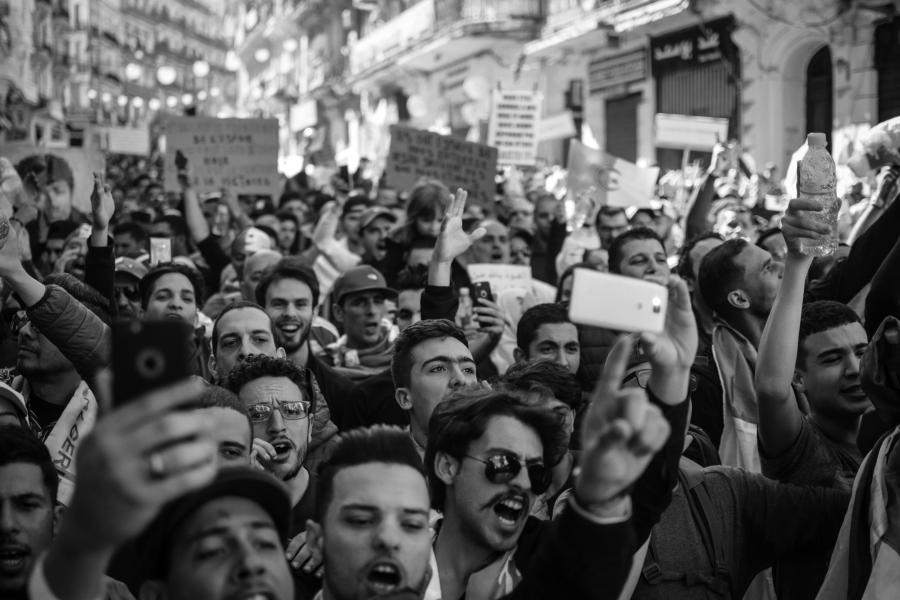 A black and white photo of a crowd of people yelling at a protest in an unspecific street.