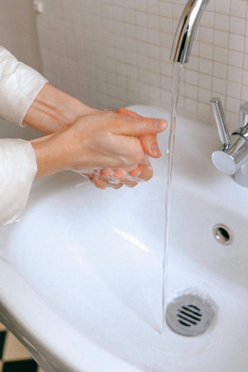 Hands being washed in a white sink with soap and running water